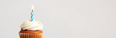 Sweet cupcake with cream frosting and a blue striped candle for a birthday celebration at a cozy indoor settingの素材