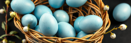 Decorative blue eggs in a woven basket with greenery on a dark background, perfect for spring festivities and celebrationsの素材