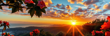 A beautiful sunset over the mountains, with bright orange and yellow clouds and a few red flowers in the foregroundの素材