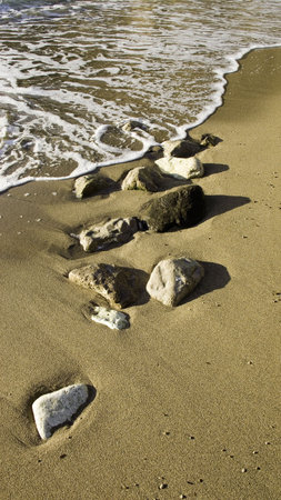 Still life of brown sandy beach with small boulders washed over by the sea