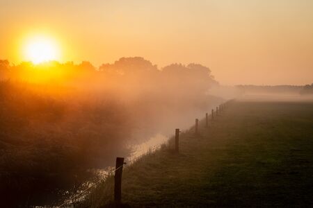 Beautiful misty morning in the Netherlands with an orange rising sun, picture tasks in the province of Overijsselの写真素材