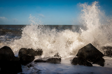 Pier at corner of Holland, with basalt blocks and splashing and foamy North Sea water in the winter time.の写真素材