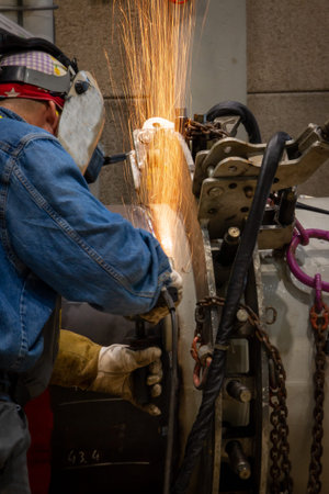 A welder grinding and welding on a metal pipe piece for industrial use