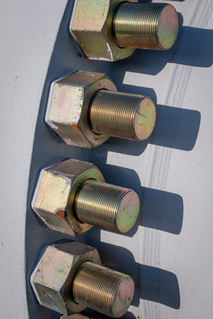 Large heavy galvanized industrial bolts and nuts mounted in a large metal flange on a pipe