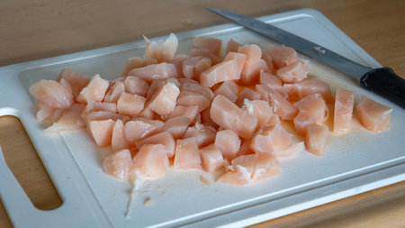 Cut chicken breast into cubes lying on a cutting board, ready to be prepared in a mealの写真素材