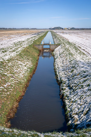 Typical Dutch landscape with meadows, snow, farms, ditches and locks to maintain the water level, province of Drenthe, the Netherlandsの写真素材