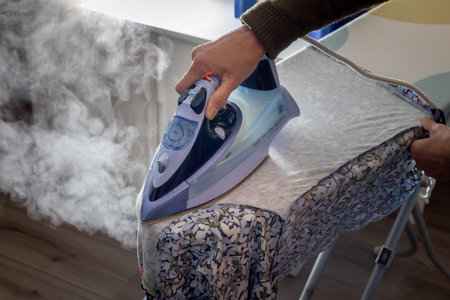 Ironing laundry with a light purple colored hot steam iron on the ironing table, photo taken in the Netherlandsの写真素材