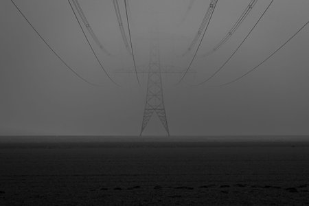 A dark misty day towards evening on the farmland with the high-voltage pylons and the high-voltage cables that are partly hidden in the mist, the Netherlands, Overijsselの写真素材