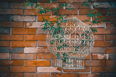 Vintage decorative birdcage covered with blooming flowers against a brick wall creating a warm and aesthetic atmosphere