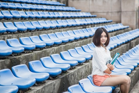 asian female student siting in the campus stadium with file folders in her handの写真素材
