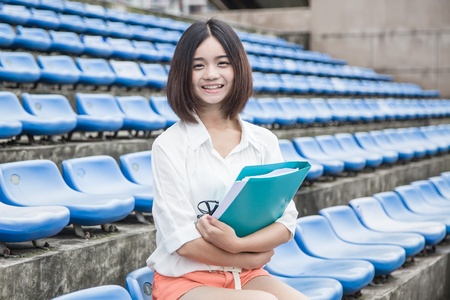 asian female student siting in the campus stadium with file folders in her handの写真素材