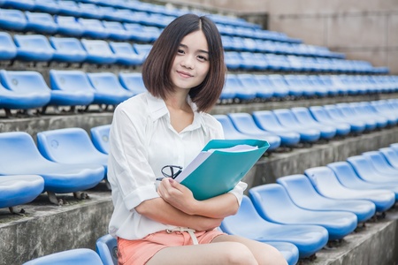 asian female student siting in the campus stadium with file folders in her handの写真素材