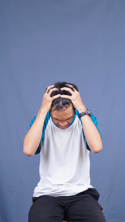 asian man stress gesture and expression holding head and hair with isolated blue backgroundの写真素材