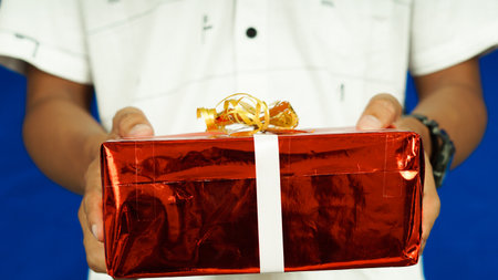 Christmass gift in red paper held hand white clothes isolated blue background, close upの写真素材