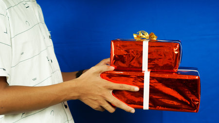Christmass gift in red paper held hand white clothes isolated blue background, close upの写真素材