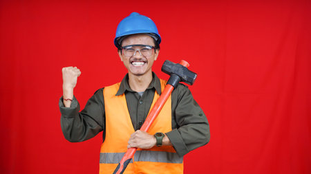 asian construction worker man wearing uniform, helmet, with hammer isolated red backgroubdの写真素材