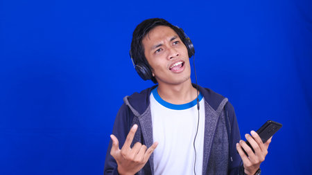 asian man listening music with happy expression wear handphone and headphone isolated blue...
