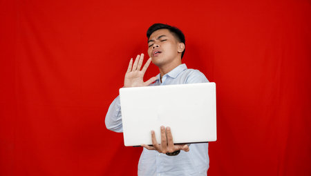 Young asian business man hiding his face with hand from laptop isolated red background
