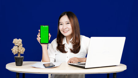 business Asian woman with green screen handphone in workspace isolated blue backgroundの写真素材