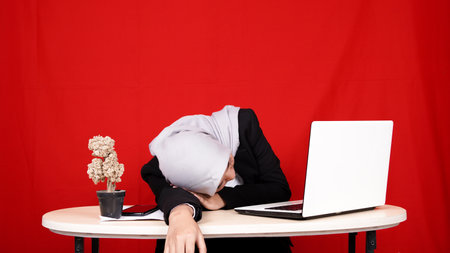 beautiful Asian business woman wearing hijab sleepy in workspace isolated blue backgroundの写真素材