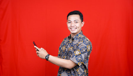 asian man excited expression view cellphone with batik clotheの写真素材