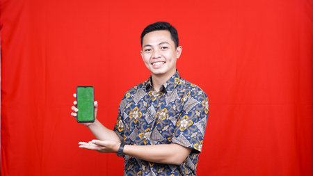 asian man with batik clothes and pointing at green screen cellphoneの写真素材
