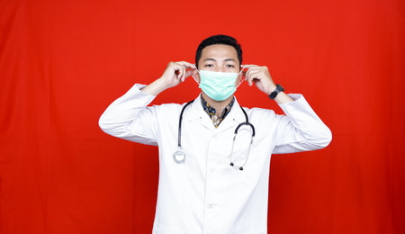 Asian Male Doctor wearing mask. Protect from virus isolated red backgroundの写真素材