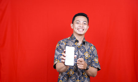 asian man with batik clothes and pointing at green screen cellphoneの写真素材
