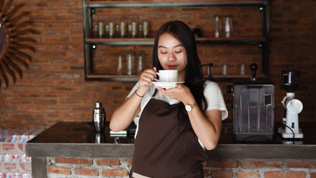 Asian Women Barista smiling and looking to camera in coffee shop counter. Barista female holding coffee cup at cafeの写真素材