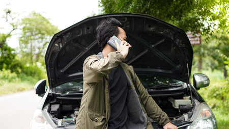 Asian man opened the hood of the car while calling
