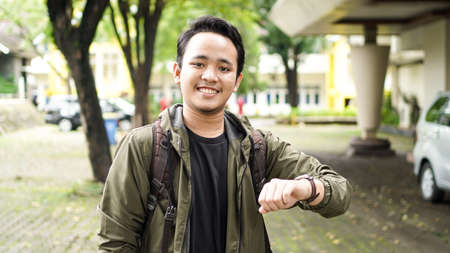 Smiling Asian man wearing a backpack is checking the timeの写真素材