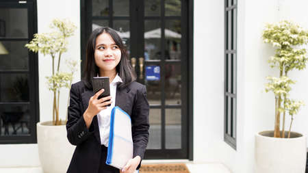 Beautiful young asian business woman in suit standing at cafe with phone and Brown envelopeの写真素材