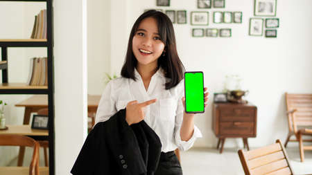 Beautiful young asian business woman in suit standing at cafe with green screen phoneの写真素材