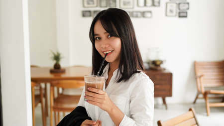 Beautiful young asian businesswoman in suit standing holding brown coffee cup in caffe while having a coffee break.の写真素材