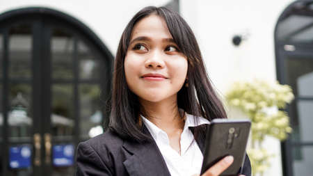 Beautiful young asian business woman in suit standing at cafe with phone and Brown envelopeの写真素材