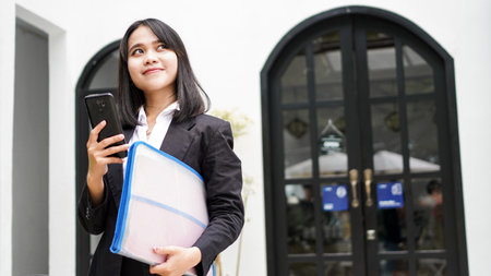 Beautiful young asian business woman in suit standing at cafe with phone and Brown envelopeの写真素材