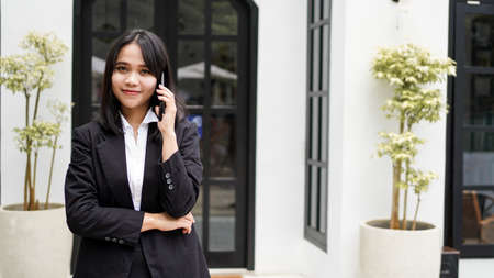 Beautiful young asian business woman in suit standing at cafe calling  with brown envelopeの写真素材