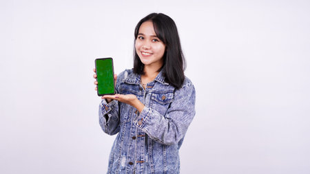 Asian women smiling wearing jeans jacket and holding green screen phone with isolated white...