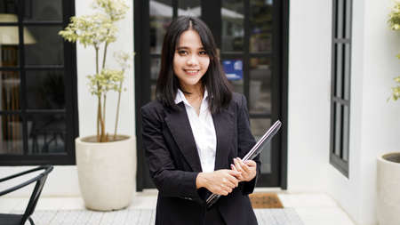 Asian business woman smiling with 
brown envelope and standing in front officeの写真素材