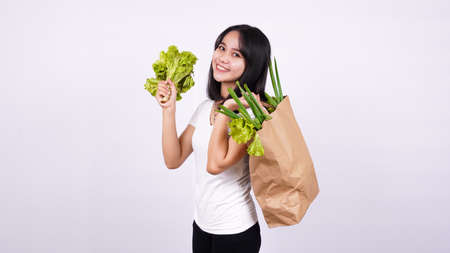 Beautiful Asian woman with paper bag of fresh vegetables and holding fresh lettuce with isolated white backgroundの写真素材