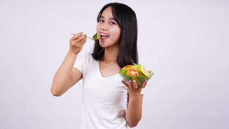 Young asian woman happy eating healthy salad with isolated white backgroundの写真素材