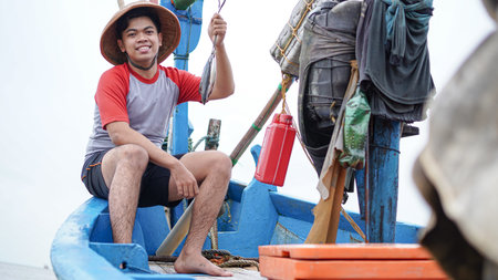 Happy young fisherman on the beach holding his catch fish and shows in front of his boat
