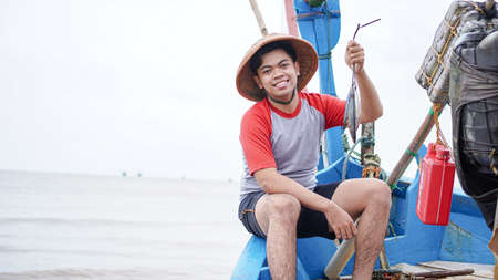 Happy young fisherman on the beach holding his catch fish and shows in front of his boatの写真素材