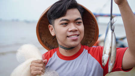 Happy young fisherman on the beach holding his catch fish and shows in front of his boatの写真素材