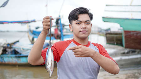 Happy young fisherman on the beach holding his catch fish and shows in front of his boatの写真素材