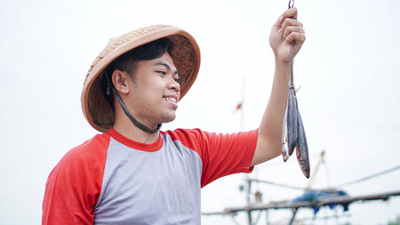 Happy young fisherman on the beach holding his catch fish and shows in front of his boatの写真素材