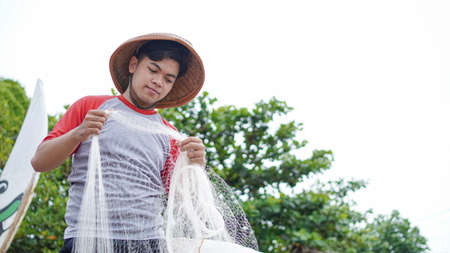 Portrait of a young male fisherman preparing a fishing net in beachの写真素材