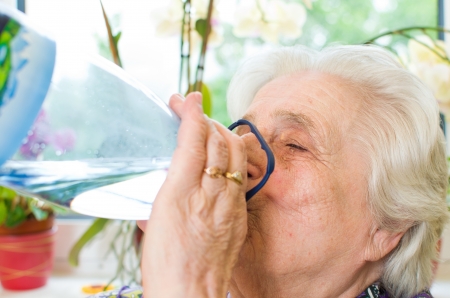 Happy old gray-haired woman drinkingの写真素材