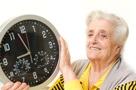 portrait of a happy senior woman holding a clock over a white backgroundの写真素材