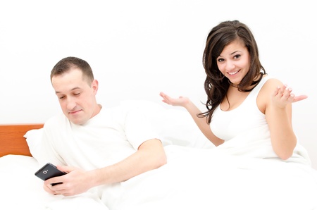 Young beautiful couple in bed, man is busy with his cell phone - woman upsetの写真素材